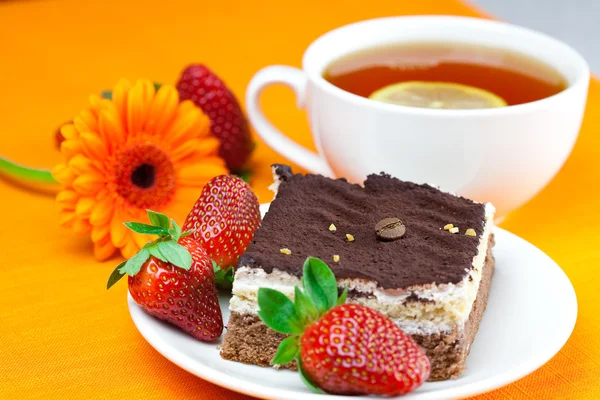 Gerbera, lemon tea, cake and strawberries lying on the orange fa — Stock Photo, Image