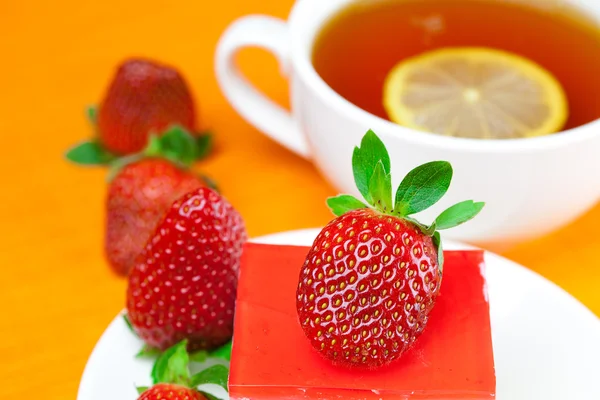 Citroenthee, cake en aardbeien op de oranje stof — Stockfoto