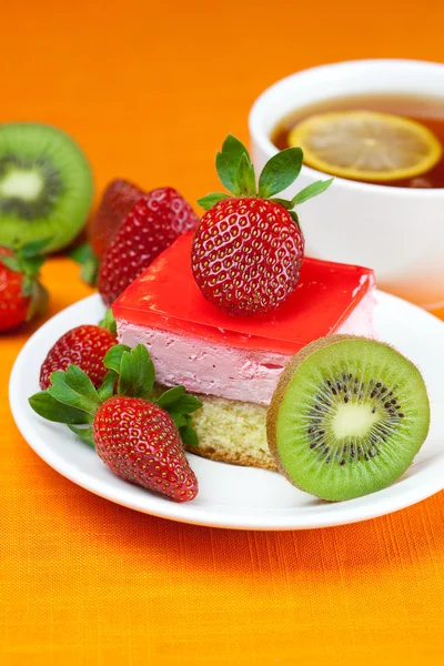 Zitronentee, Kiwi, Kuchen und Erdbeeren liegen auf dem orangefarbenen Stoff — Stockfoto