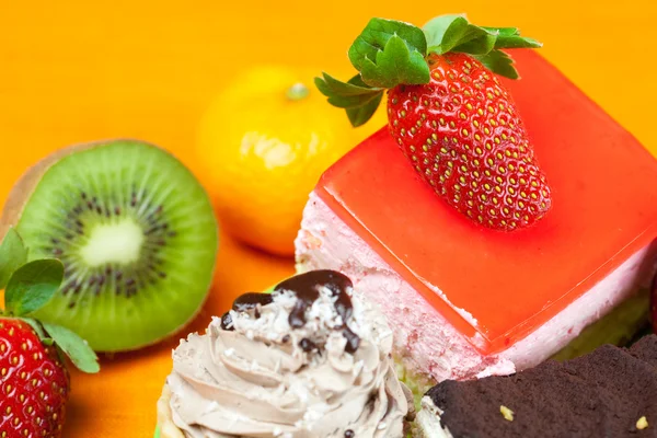Mandarine, Kiwi, Kuchen und Erdbeeren liegen auf dem orangefarbenen Stoff — Stockfoto