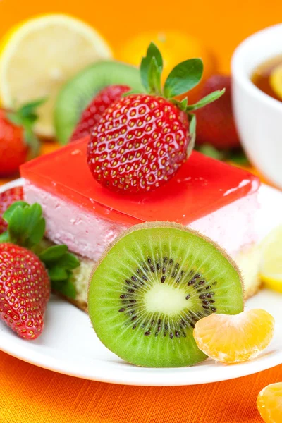 Zitronentee, Kiwi, Kuchen und Erdbeeren liegen auf dem orangefarbenen Stoff — Stockfoto
