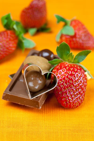 Chocolate bars, strawberry, heart and the candy on the orange fa — Stock Photo, Image