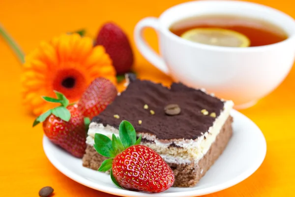 Gerbera, lemon tea, cake and strawberries lying on the orange fa — Stock Photo, Image