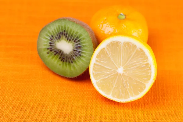 Kiwi, cytryna, mandarynka, leżącego na pomarańczowym tkaniny — Zdjęcie stockowe