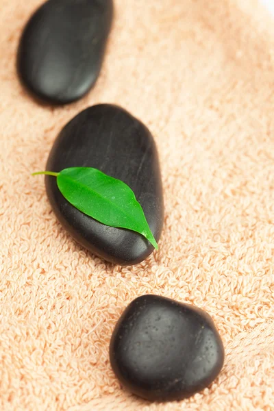 Yeşil yaprak ve bir damla su çekici üzerinde siyah spa taşlarla — Stok fotoğraf