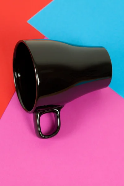 Una taza negra acostada sobre un fondo colorido —  Fotos de Stock