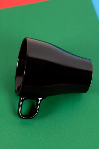 Una tazza nera sdraiata su sfondo colorato — Foto Stock
