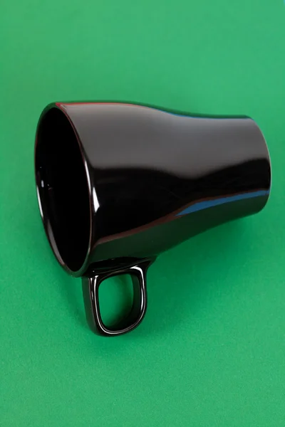 Una taza negra tumbada sobre fondo verde — Foto de Stock