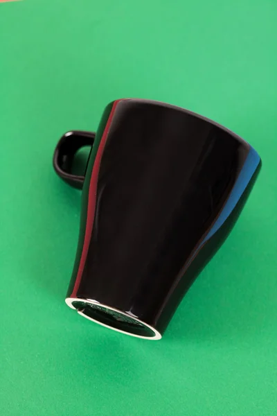Uma xícara preta deitada no fundo verde — Fotografia de Stock