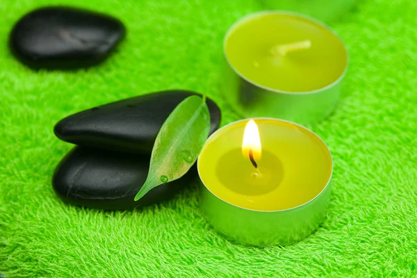 Hořící svíčku a lázeňské černé kameny, ležící na ručník — Stock fotografie