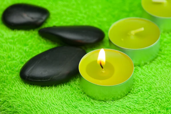 Brennende Kerze und schwarze Steine auf dem Handtuch liegend — Stockfoto