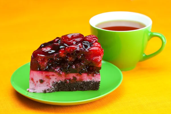Schöner Kuchen mit Beeren auf einem Teller und einer Tasse Tee auf dem o — Stockfoto