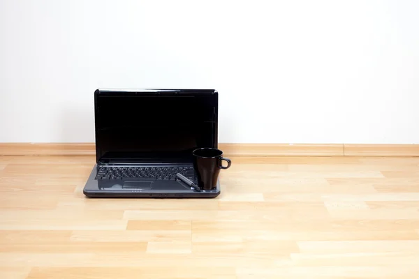 Laptop a pohár stojící na podlaze v pokoji — Stock fotografie