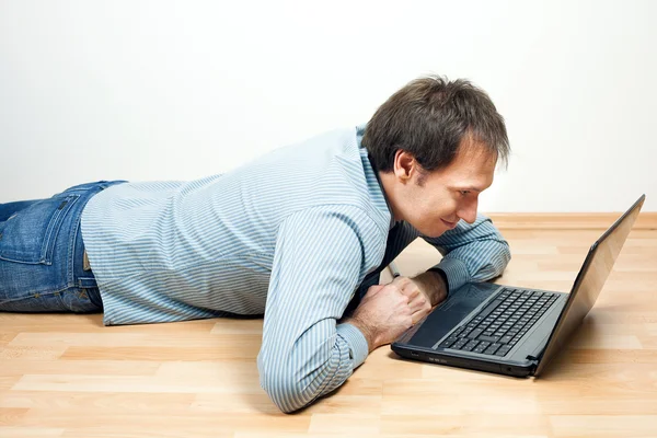 Mladý muž přes notebook leží na podlaze v pokoji — Stock fotografie