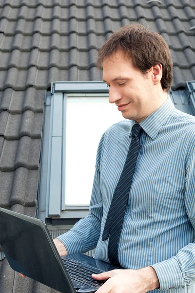 Karşı pencere ve çatı bir dizüstü bilgisayar kullanan genç adam — Stok fotoğraf