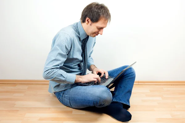 Mladý muž pomocí přenosného počítače sedí na podlaze v pokoji — Stock fotografie