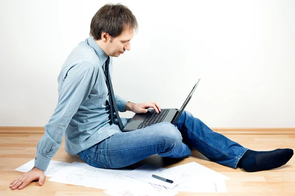 Ung man använder laptop sitter på golvet i rummet — Stockfoto
