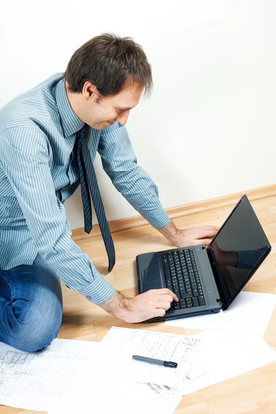 Hombre joven usando el ordenador portátil sentado en el suelo en la habitación —  Fotos de Stock