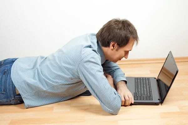 Ung man använder laptop liggande på golvet i rummet — Stockfoto