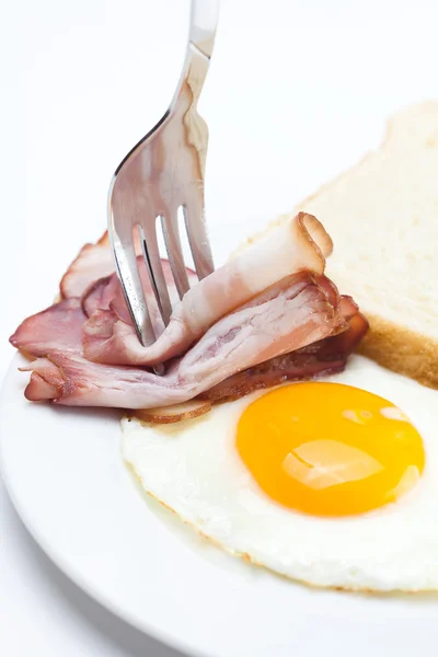 Бекон с жареными яйцами на тарелке, вилка и хлеб изолированы на w — стоковое фото