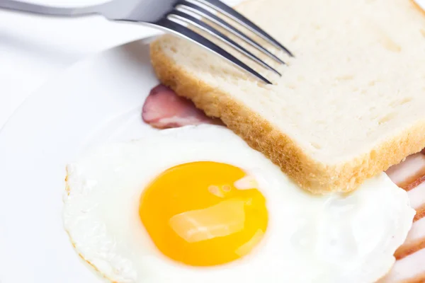 Slanina se smaženými vejci na talíř, vidlice a chléb izolovaných na w — Stock fotografie
