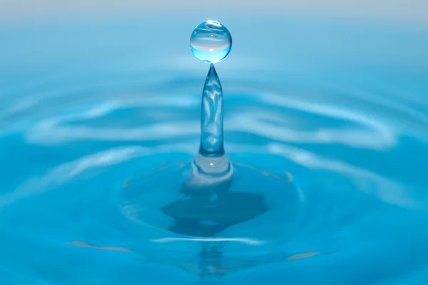 Goccia d'acqua e spruzzi su uno sfondo blu — Foto Stock
