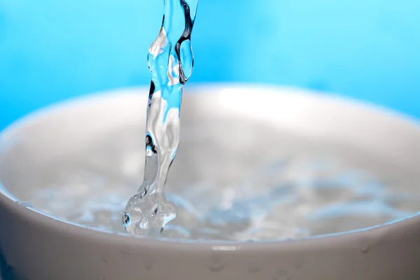 Spruzzi d'acqua in una tazza su uno sfondo blu — Foto Stock