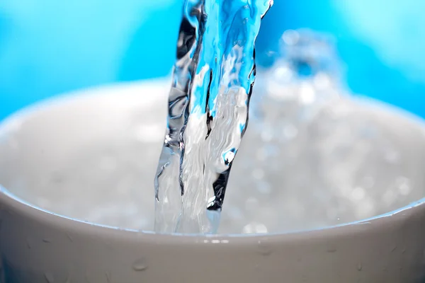 Stříkající vody v šálku na modrém pozadí — Stock fotografie