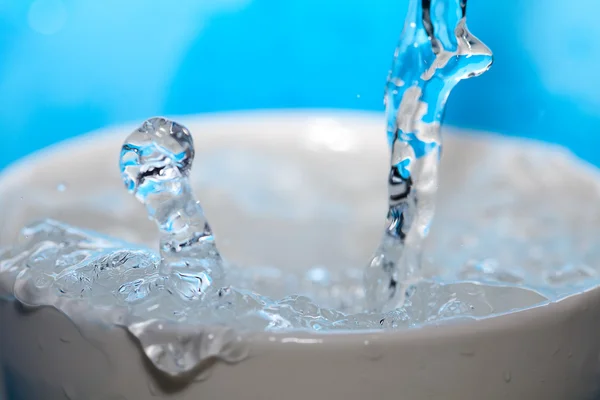 Брызги воды в чашке на синем фоне — стоковое фото