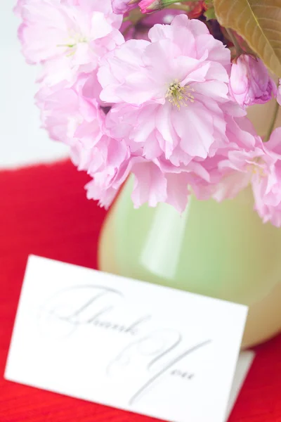 Sakura fleur dans un vase et une carte signée merci sur un bac rouge — Photo