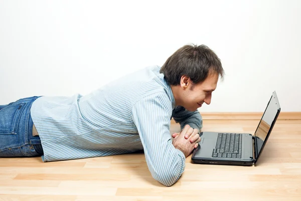 Jonge man met behulp van laptop liggend op de vloer in de kamer Stockfoto