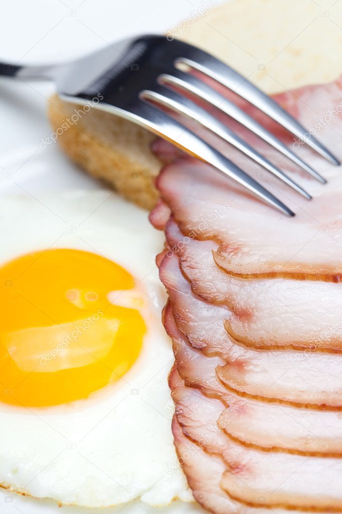 Bacon with fried eggs on a plate, fork and bread isolated on w
