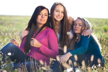 gökyüzü backg alanda oturan üç genç güzel kadın