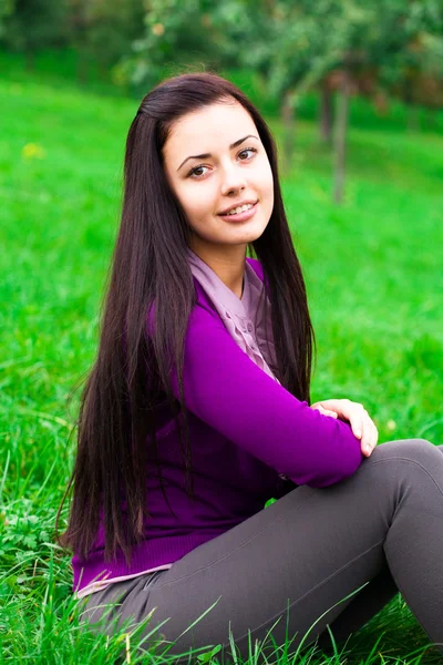 Yeşil çimenlerin üzerinde oturan güzel genç kadın — Stok fotoğraf