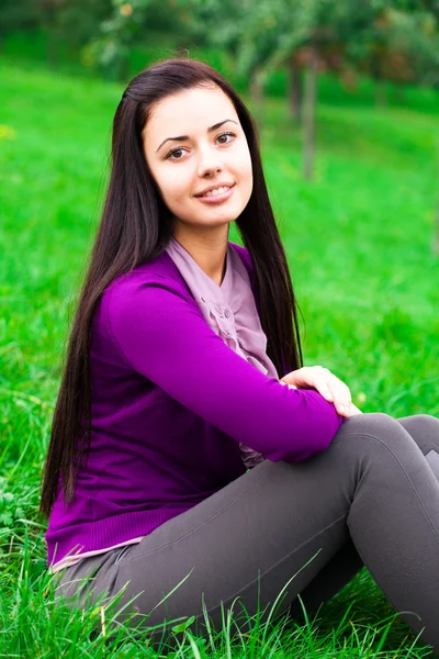 Piękna młoda kobieta siedzi na zielonej trawie — Zdjęcie stockowe