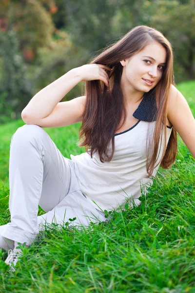 Piękna młoda kobieta siedzi na zielonej trawie — Zdjęcie stockowe