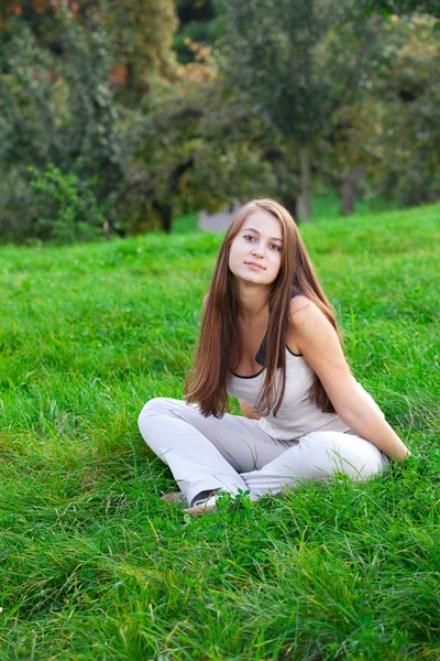 美しい若い女性は緑の芝生の上に座って — ストック写真