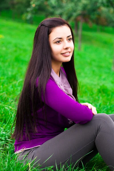 Vacker ung kvinna som sitter på grönt gräs — Stockfoto