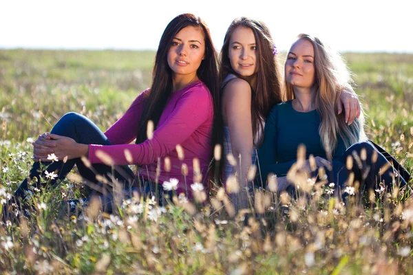 Tre unga vackra kvinnan sittande i ett fält på himlen backg — Stockfoto