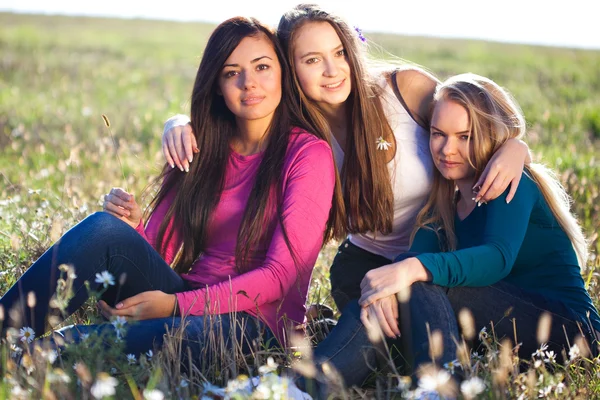 Tre unga vackra kvinnan sittande i ett fält på himlen backg — Stockfoto