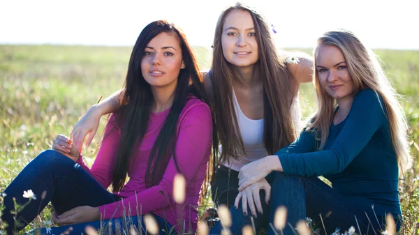 Tři mladá krásná žena, sedící v poli na pozadí oblohy — Stock fotografie
