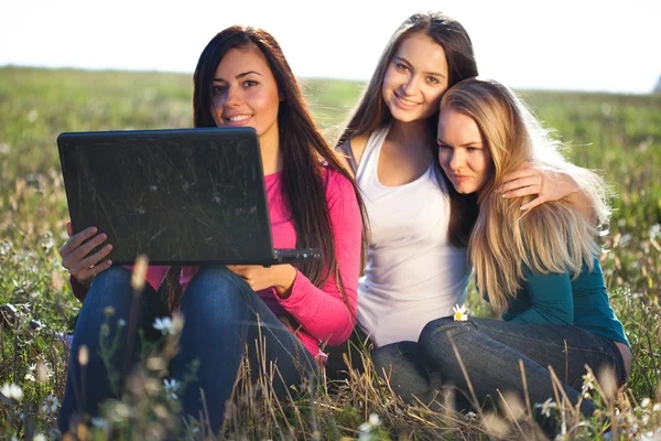 Tre giovani bella donna con un computer portatile seduto nel campo o — Foto Stock