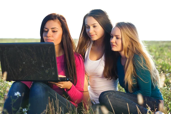 Drie jonge mooie vrouw met een laptop zitting in het veld o — Stockfoto