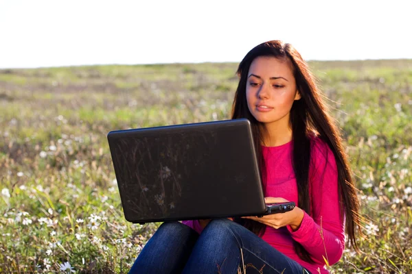 Jonge mooie vrouw met een laptop zitting in het veld op sky — Stockfoto