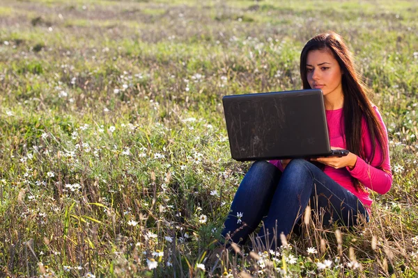 Jonge mooie vrouw met een laptop zitting in het veld op sky — Stockfoto