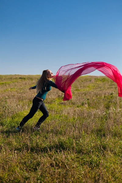 Joven hermosa mujer saltando con tejido en el campo contra — Foto de Stock