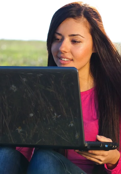 年轻漂亮的女人和一台笔记本电脑，坐在天空上的字段 — 图库照片