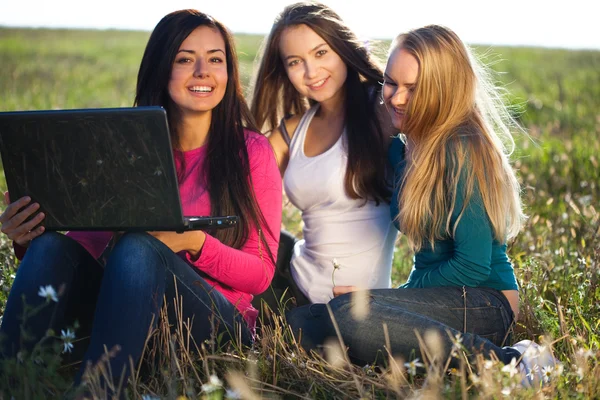 Trois jeunes belles femmes avec un ordinateur portable assis dans le champ o — Photo