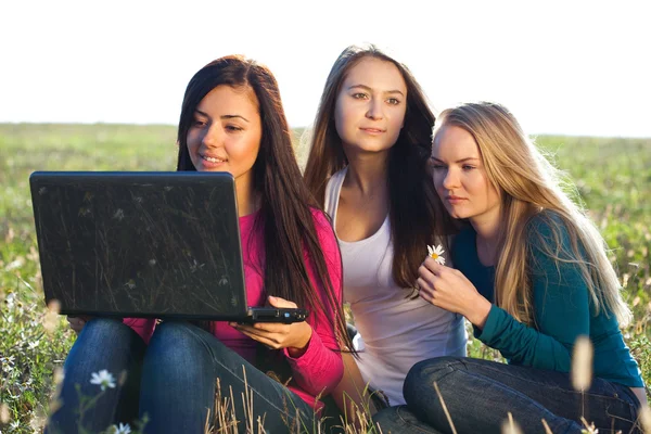 Drei junge schöne Frau mit einem Laptop sitzt auf dem Feld o — Stockfoto