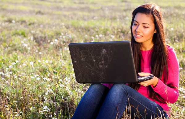 Jovem mulher bonita com um laptop sentado no campo no céu — Fotografia de Stock